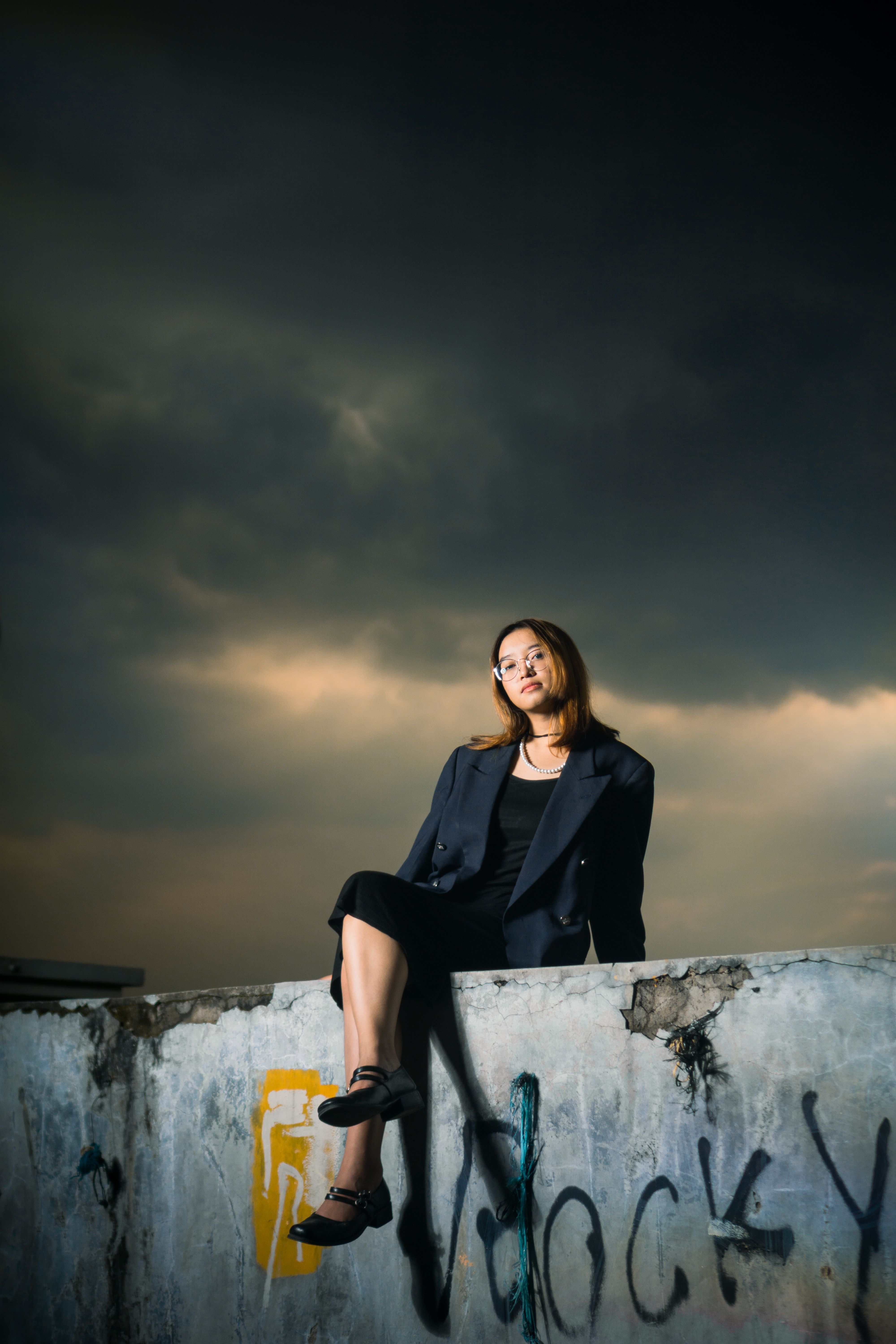 Stylish woman posing on a graffiti-covered wall under dramatic skies.