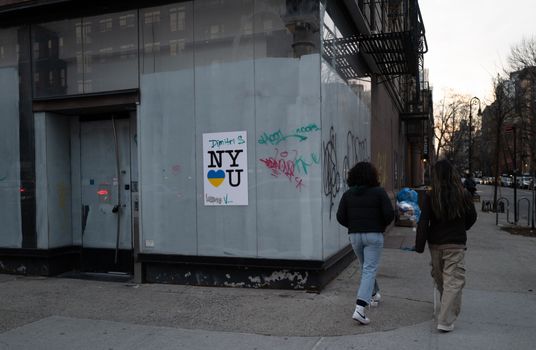 Two people walking past a building with graffiti in an urban setting at dusk.