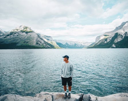 A man standing on a rock overlooking a beautiful lake with snow-covered mountains in Banff, Canada.