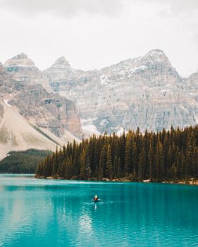 A serene scene of a canoeist on Moraine Lake with majestic Rocky Mountains in the background.