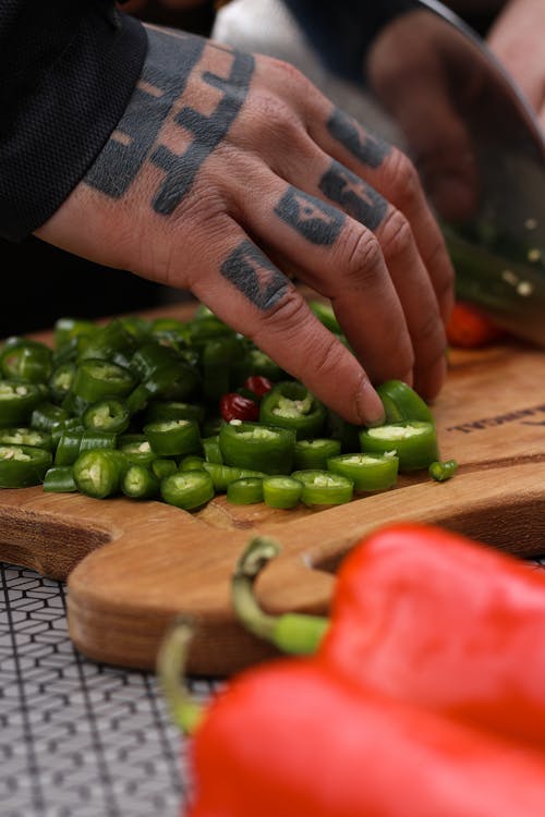 Free A Tattooed Person Holding a Green Chili Peppers on a Wooden Chopping Board Stock Photo