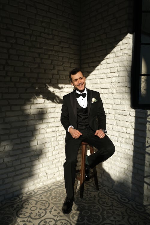 A Good-Looking Man in Black Suit Sitting on a Stool