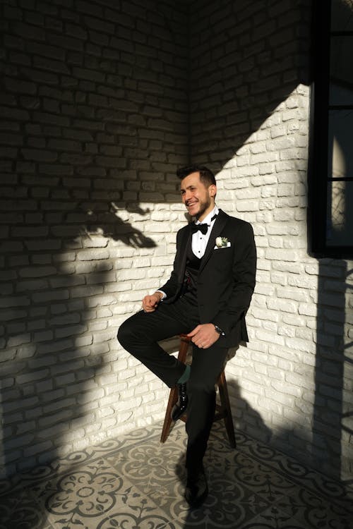 A Good-Looking Man in Black Suit Sitting on a Stool