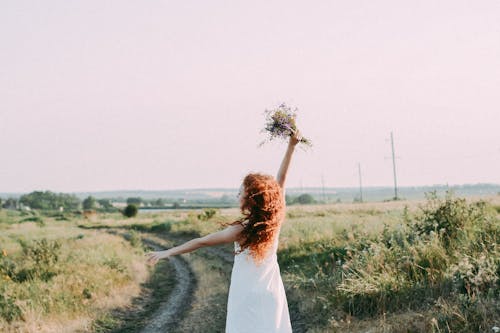 Woman in Dress with a Bouquet of Flowers on the Country Road 