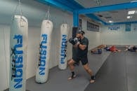 Man in Black T-shirt and Black Shorts Standing Beside White and Blue Boxing Gloves