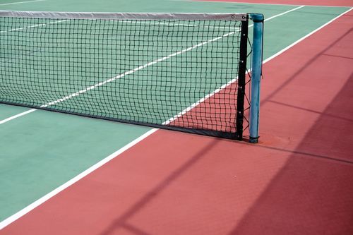 Free Detailed view of a tennis net on a vibrant outdoor court with sunlight and shadows. Stock Photo