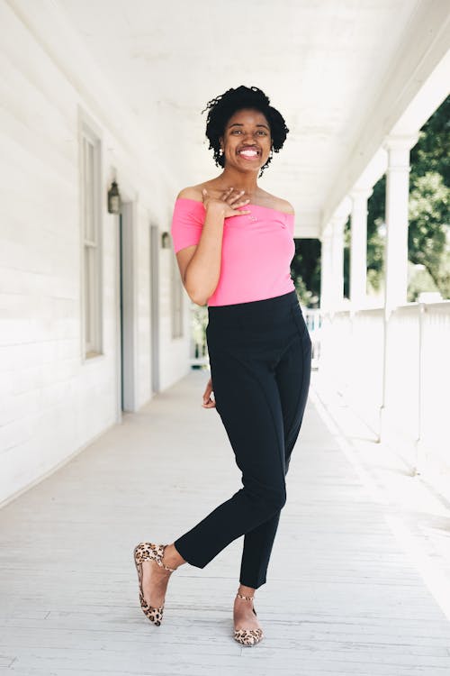 Mulher Vestindo Camisa Rosa Com Ombro E Calça Preta Em Pé Perto Da Parede