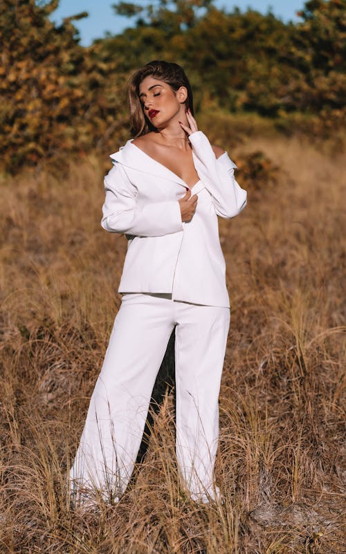 A Woman in White Blazer and White Pants Posing on a Grassy Field