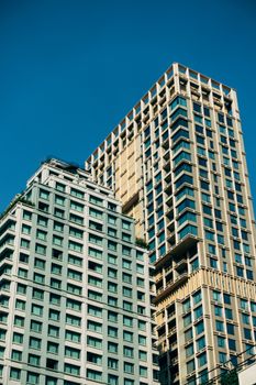Low angle view of two modern high-rise buildings with glass facades under a clear blue sky.