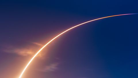 A stunning rocket launch leaving a bright arc above a beach with onlookers.