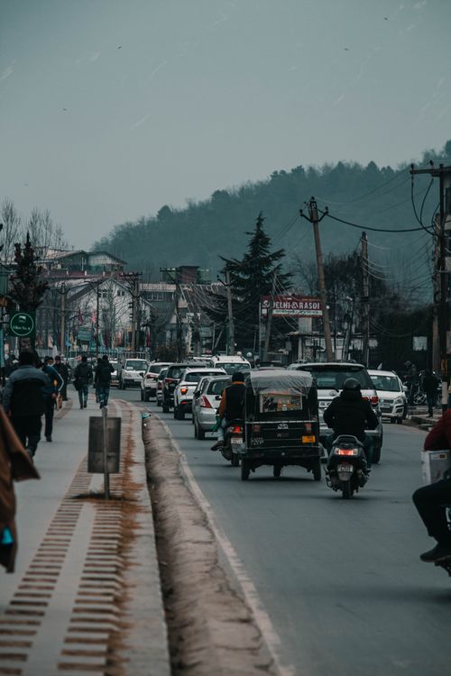 Free Busy street scene in Srinagar, Kashmir featuring vehicles and pedestrians against a mountain backdrop. Stock Photo
