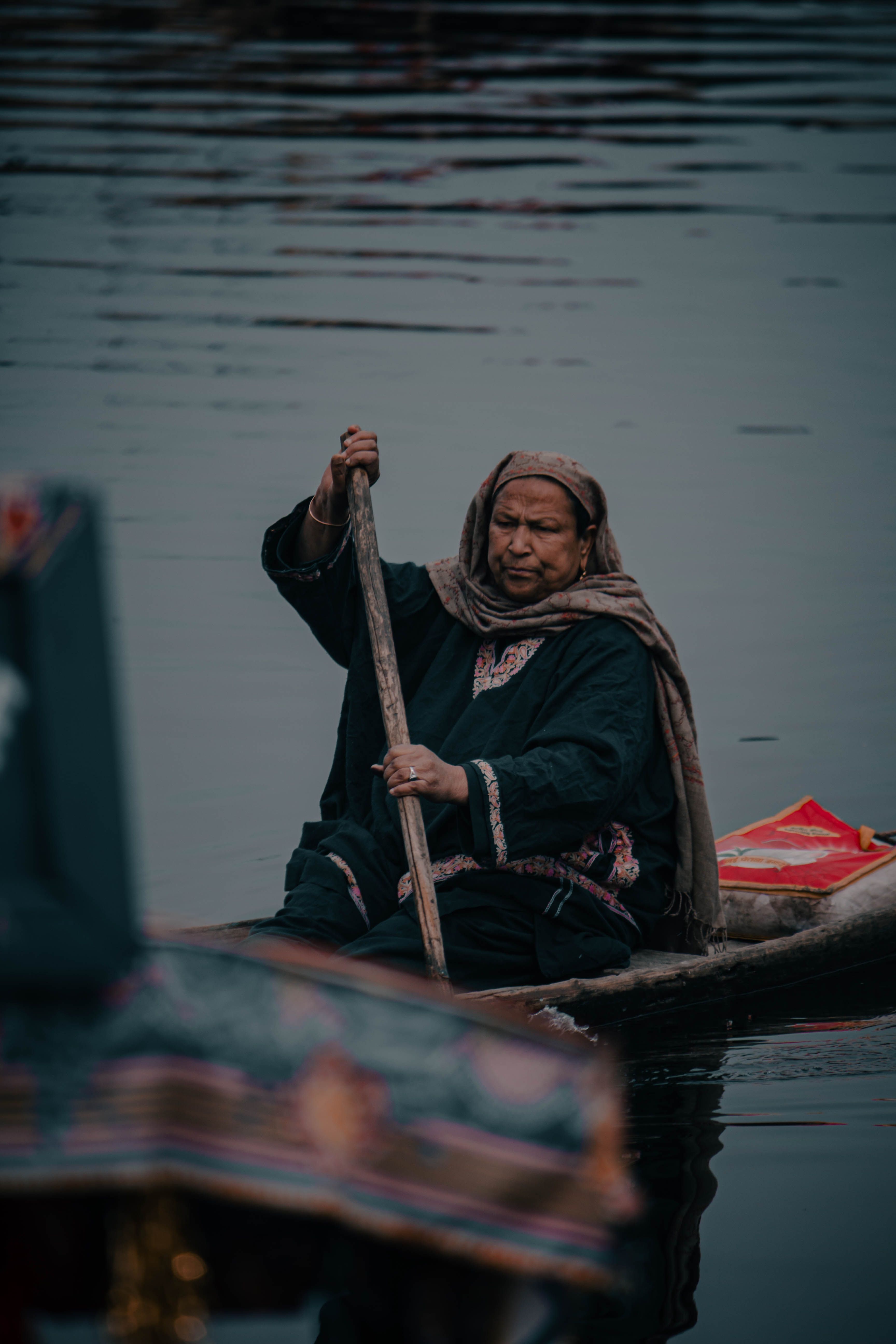 Traditional Kashmiri woman rowing a boat on serene Dal Lake in Srinagar, showcasing cultural heritage.