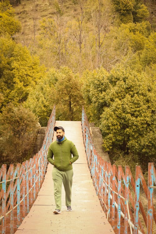 A Man in Green Jacket and Pants Walking on the Bridge