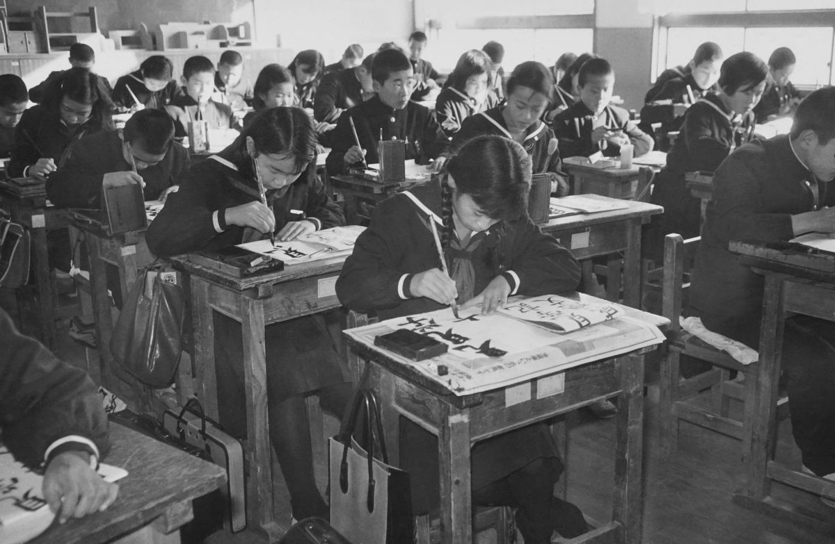 East Asian students writing calligraphy in Japanese school classroom