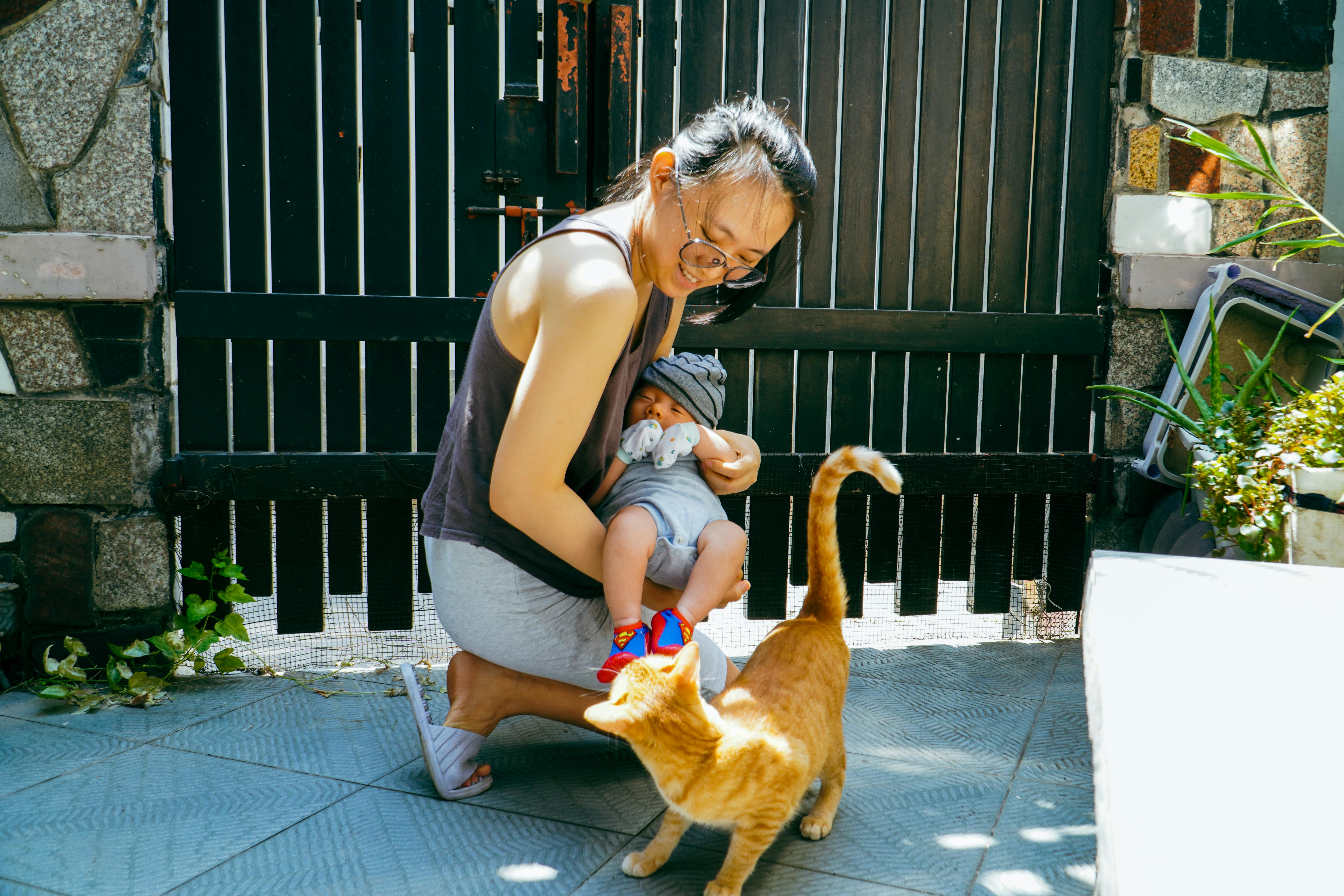 woman in black tank top carrying a baby near cat