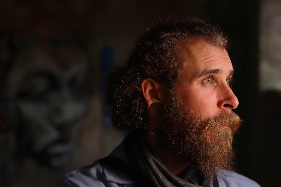 Portrait of a bearded man with intense gaze in soft lighting, creating a moody and artistic effect.