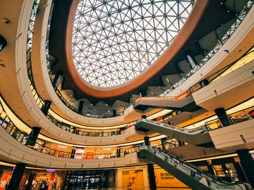 Free Wide-angle view of a futuristic shopping mall interior featuring a geometric glass ceiling and multiple levels. Stock Photo