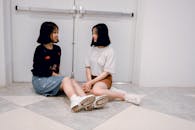 两个年轻女子在室内微笑着坐在地板上聊天