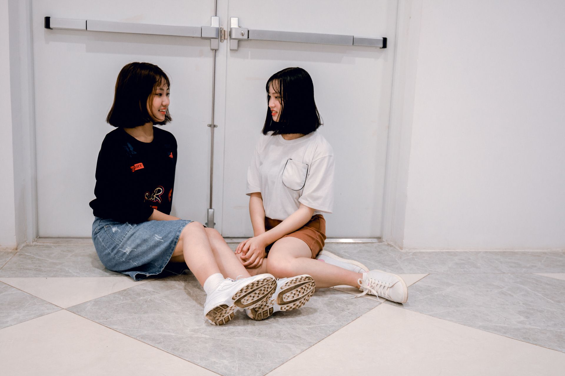 Two young women sitting on the floor chatting and smiling indoors.