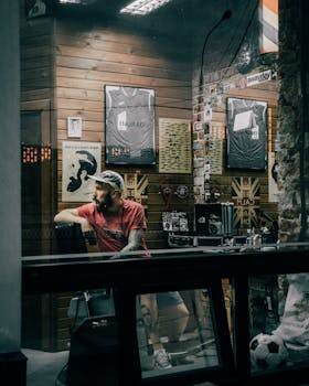 Man in casual wear sitting in trendy barbershop with posters and jerseys on the wall.