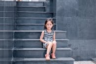 一个年轻女孩穿着条纹连衣裙，坐在光滑的灰色楼梯上，看着镜头