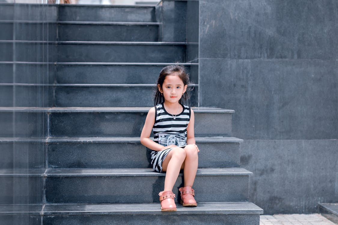 Kostenlos Mädchen, Das Gestreiftes Schwarzweiss Kleid Trägt, Das Auf Treppe Sitzt Stock-Foto