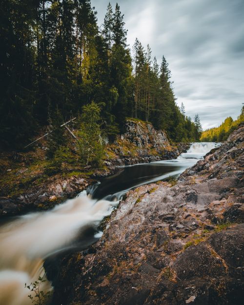 Free A tranquil river cascades through a lush forest, surrounded by rocky terrain. Stock Photo