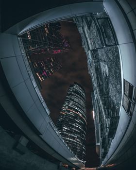Low-angle view of illuminated skyscrapers at night through an urban archway.