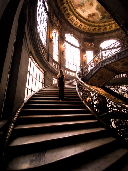 A solitary figure ascends a grand staircase inside a historic building in Mexico City.