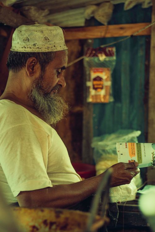 Free Side view of a bearded shopkeeper in Bangladesh reading a leaflet in his store. Stock Photo