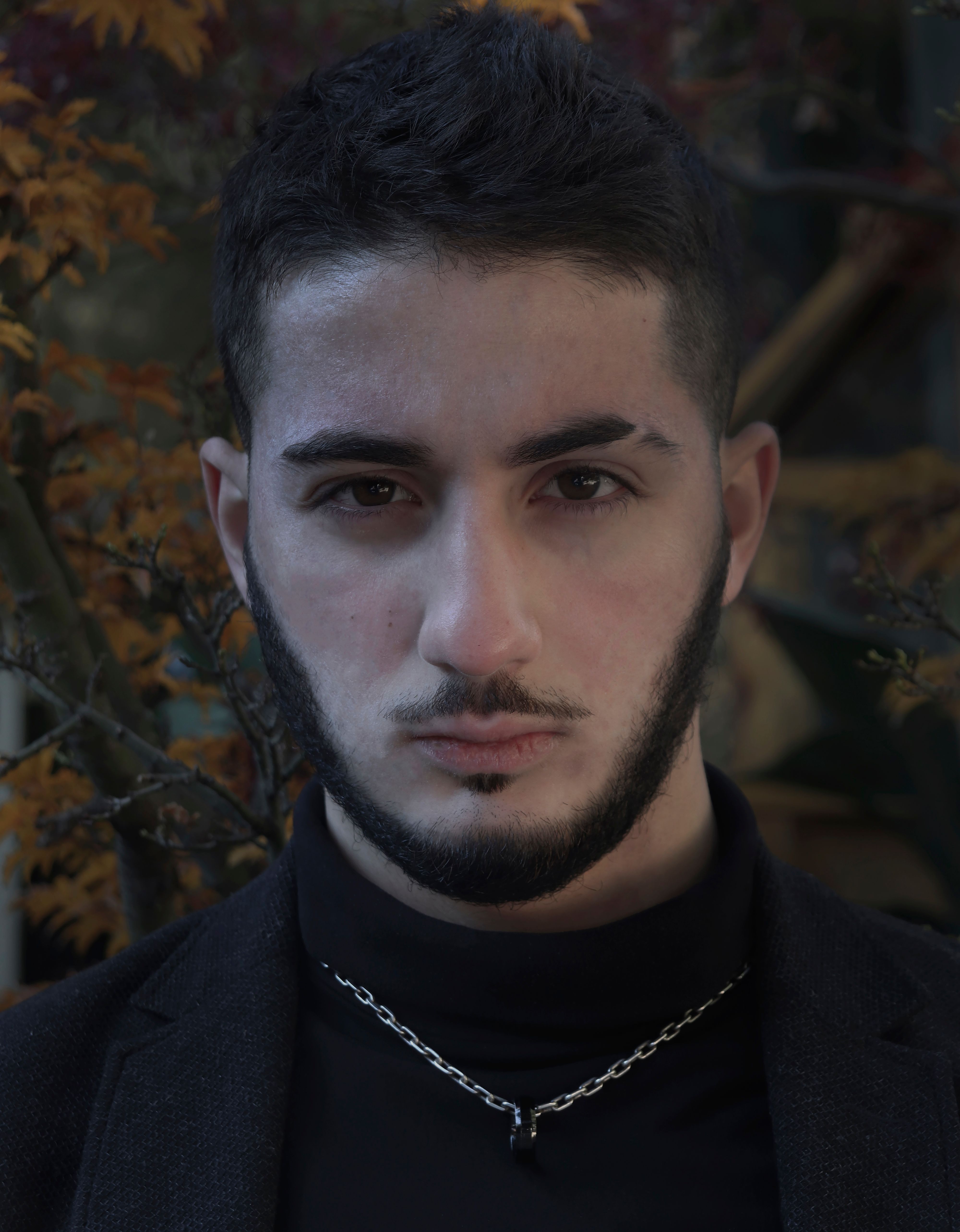 A moody portrait of a bearded man outdoors with an intense expression.
