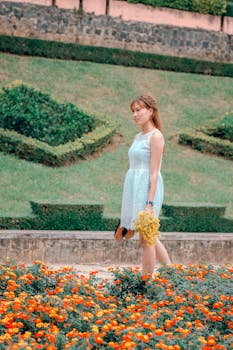 一名年轻女子身穿夏装，手捧鲜花，走过一个充满活力的花园
