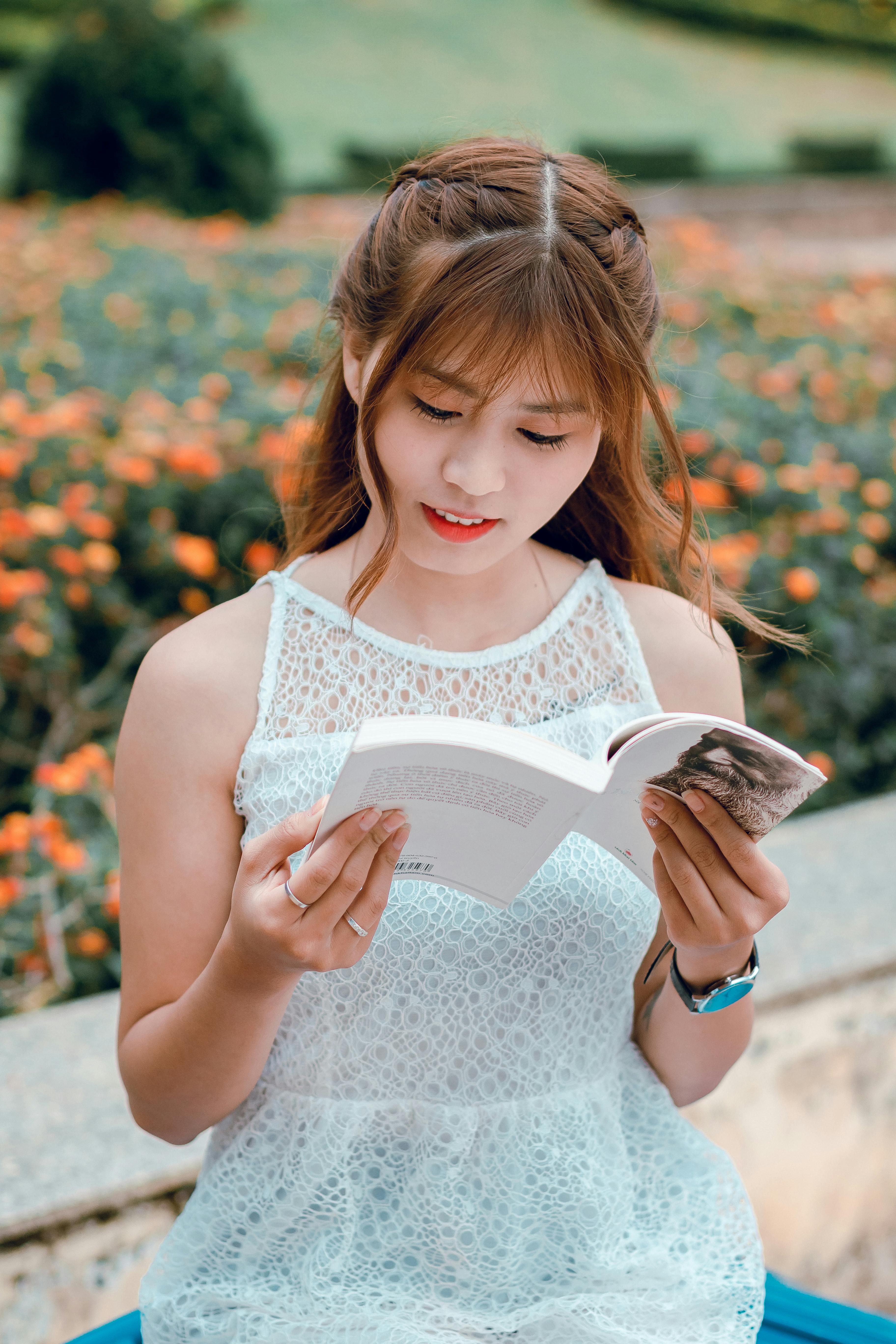 A young woman enjoying a book outdoors surrounded by flowers and greenery.