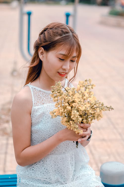 女人穿着白色蕾丝连衣裙，拿着黄色的花花束