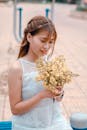 白天，一位身穿白色连衣裙的年轻女子手持黄色花朵坐在户外