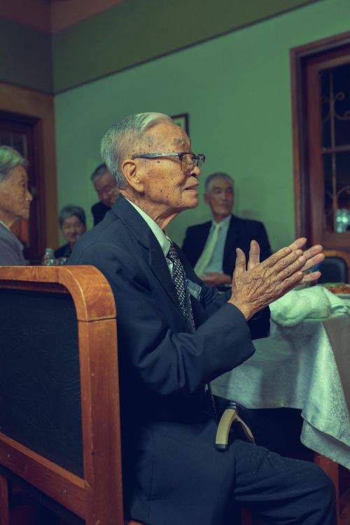 Free Senior man in suit clapping at a family dinner indoors with others seated. Stock Photo