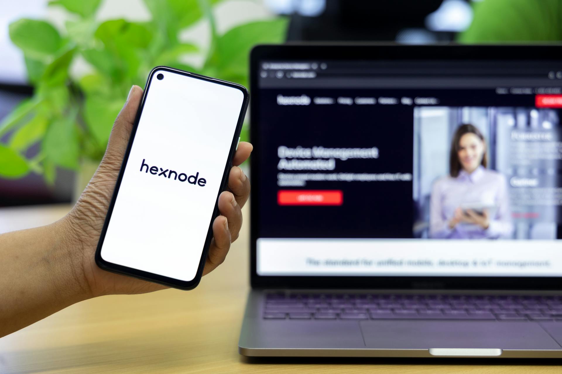 A close-up of a smartphone showing a mobile management app in front of a laptop screen.