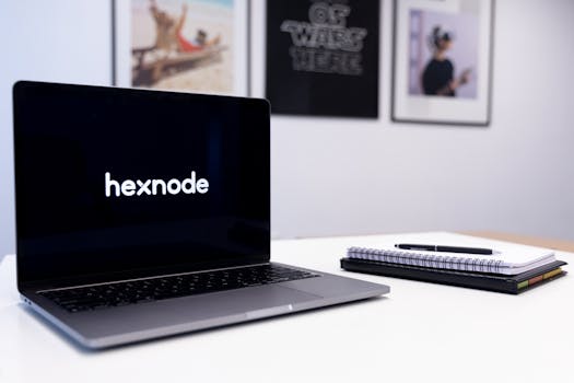 Close-up of a laptop displaying 'hexnode' on screen beside a notebook and pen on a desk.