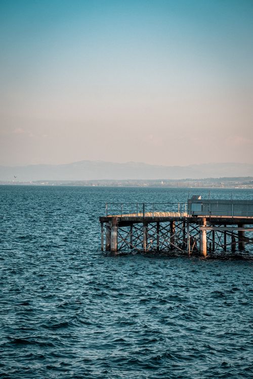 Free A serene scene of a wooden dock extending over a calm sea against a clear sky. Stock Photo