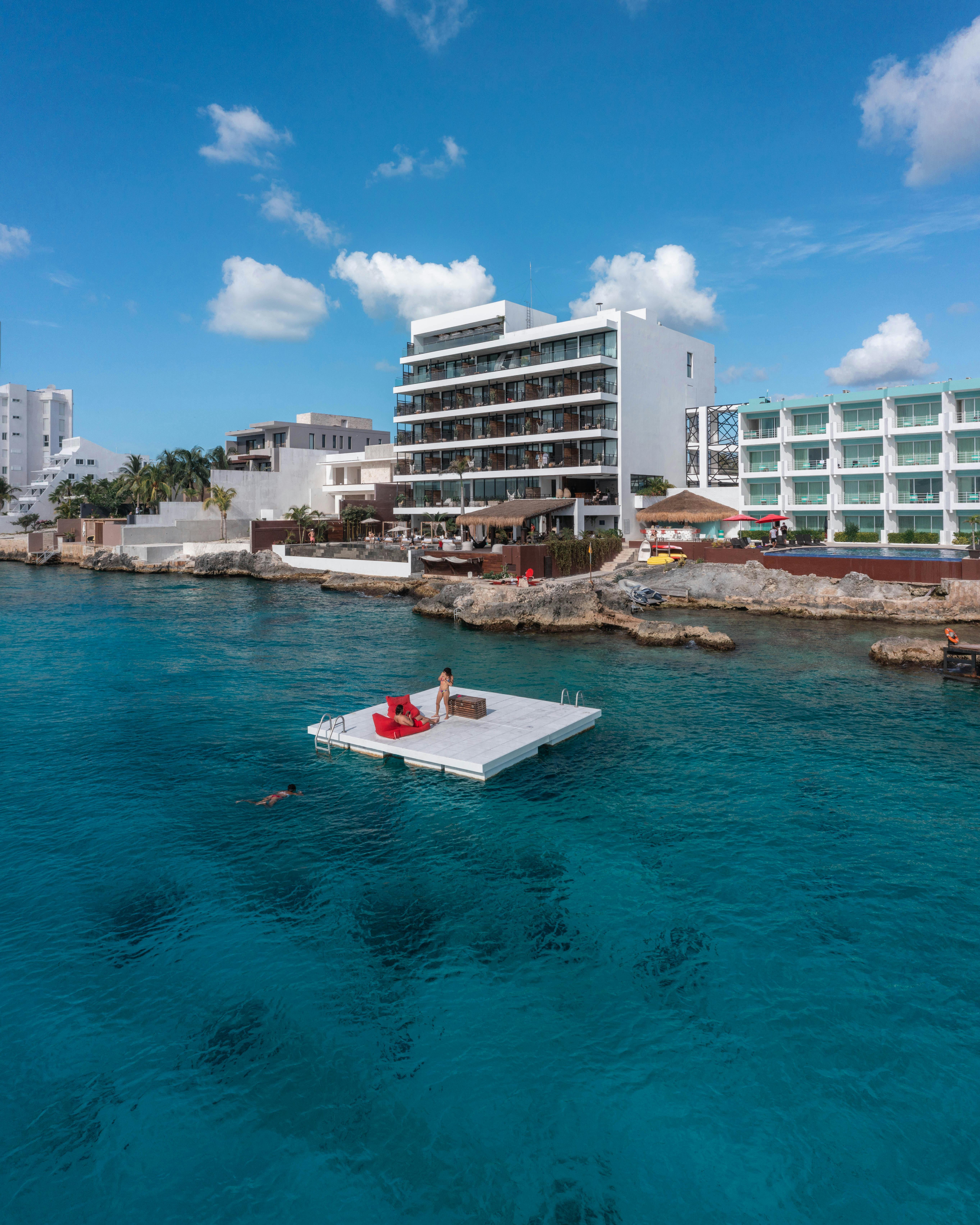 Explore a luxurious coastal resort with a floating platform on pristine blue waters under a clear sky.