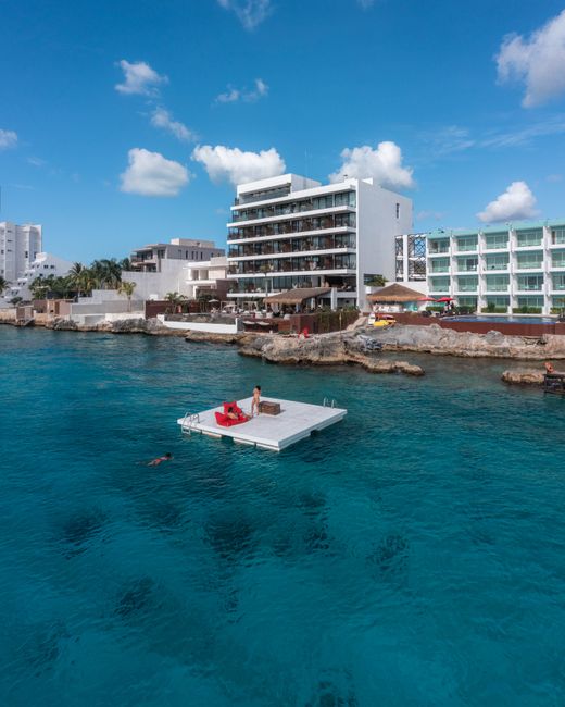 Explore a luxurious coastal resort with a floating platform on pristine blue waters under a clear sky.