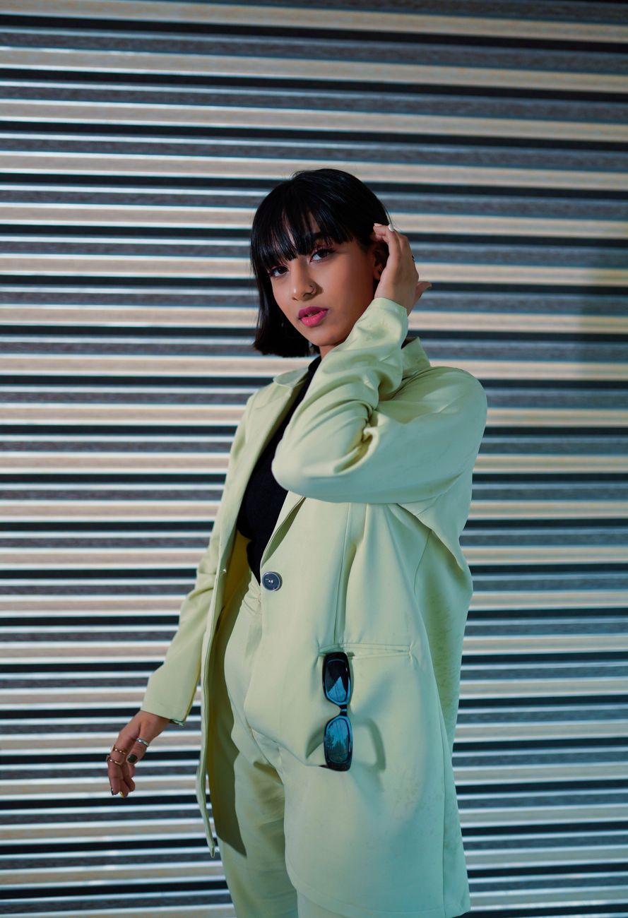 Confident woman posing in a stylish green blazer with sunglasses accessory. Modern fashion portrait.