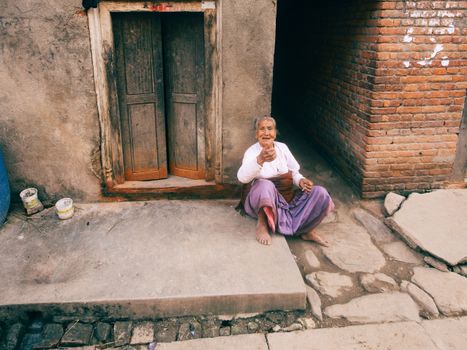 Elderly woman sitting on a sidewalk in an urban setting, looking at the camera.