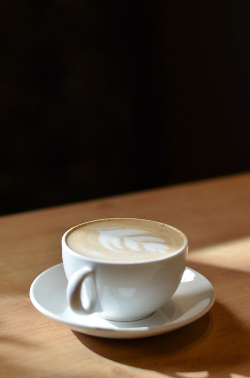 Free Close-up of a cappuccino with latte art in a white cup and saucer on a wooden table. Stock Photo