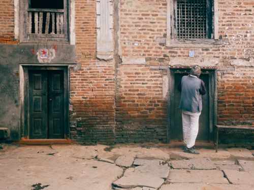 Free Man wearing casual attire enters a small, adorned wooden doorway in a rugged brick building. Stock Photo
