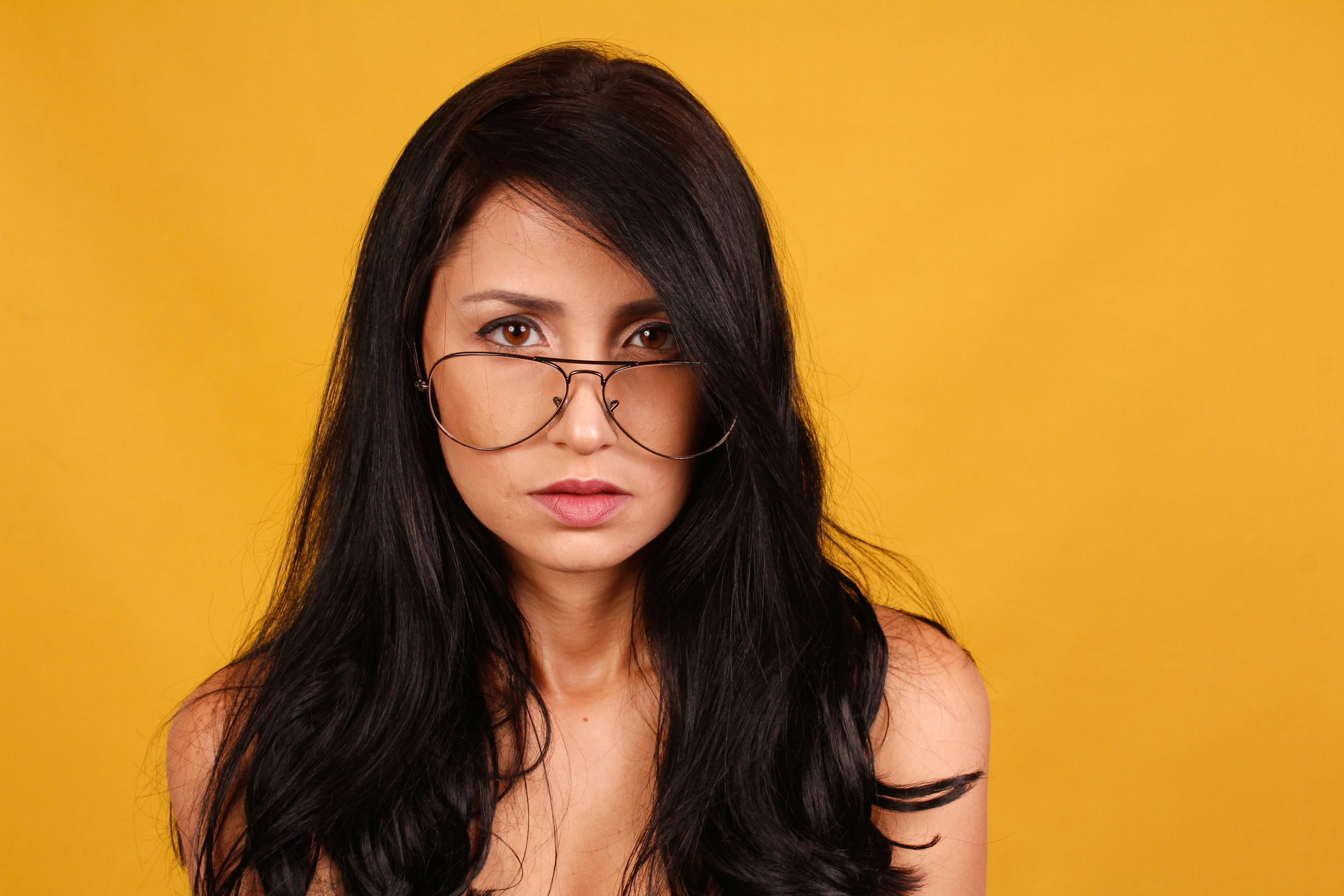 一位戴眼镜的女性以充满活力的黄色背景为衬托，引人注目地呈现肖像