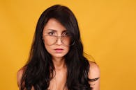 一位戴眼镜的女性以充满活力的黄色背景为衬托，引人注目地呈现肖像