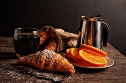 Free Enjoy a warm breakfast with fresh croissants, coffee, and orange slices on a rustic wooden table. Stock Photo