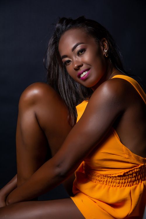 Free Studio portrait of a smiling woman in a vibrant orange outfit against a dark background. Stock Photo