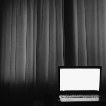 Monochrome photo of a laptop in front of a curtain, evoking a minimalist work environment.
